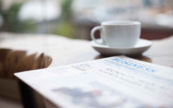 Business section of newspaper sitting on desk next to white cup and saucer.