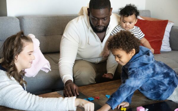 Man holding baby while playing with toddler and woman in living room.