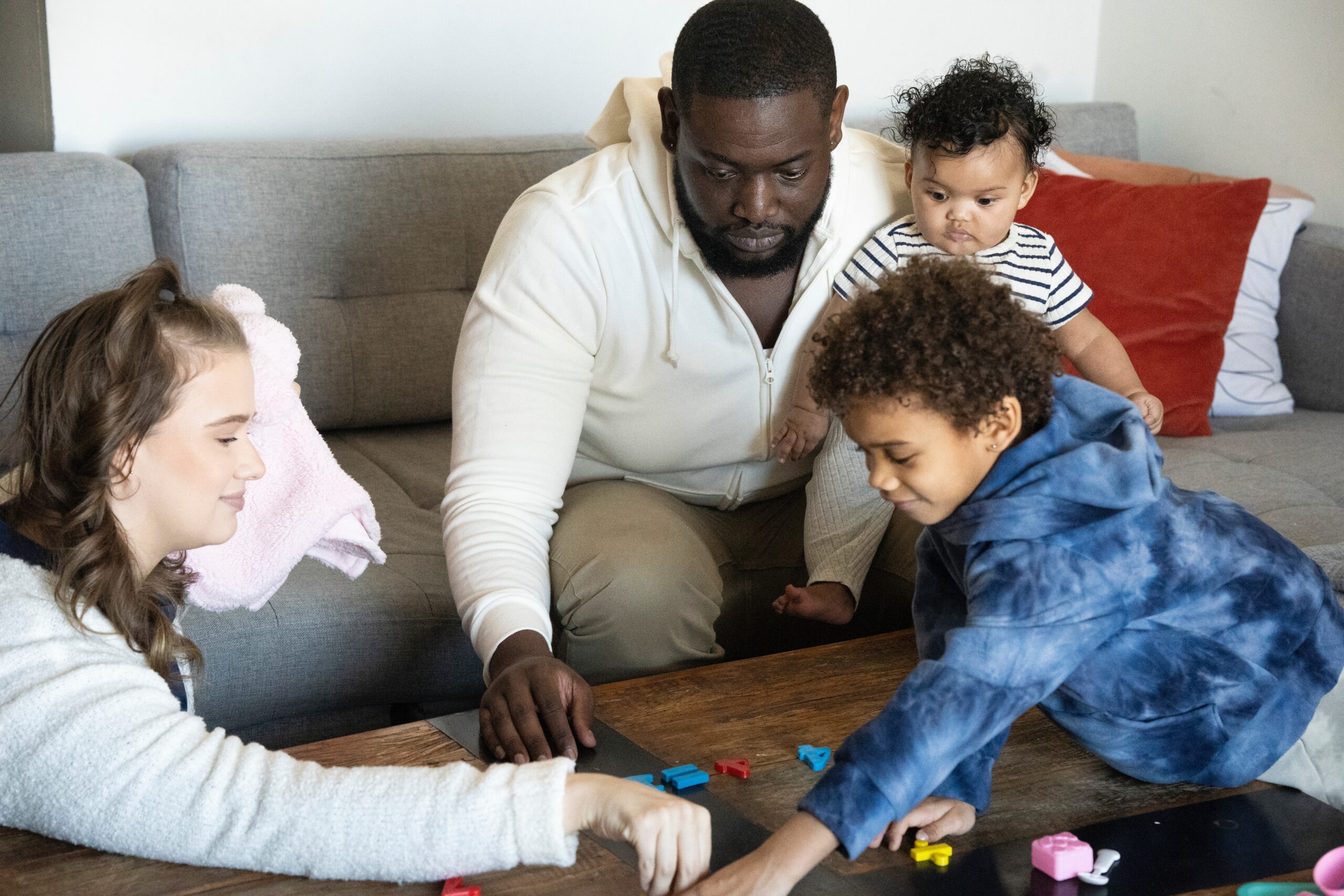 Man holding baby while playing with toddler and woman in living room.