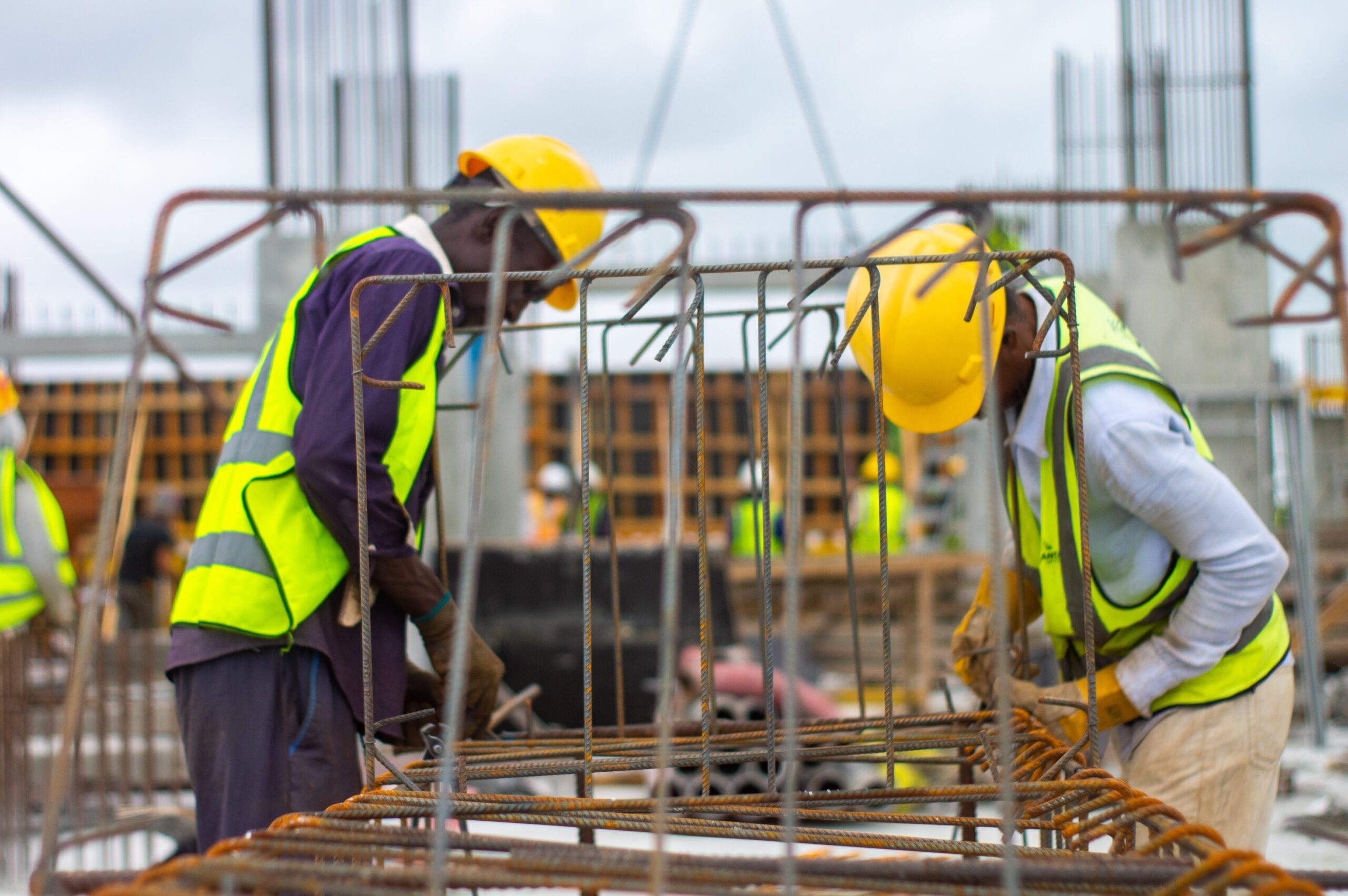 Two construction workers wearing yellow hard hats working at construction site.