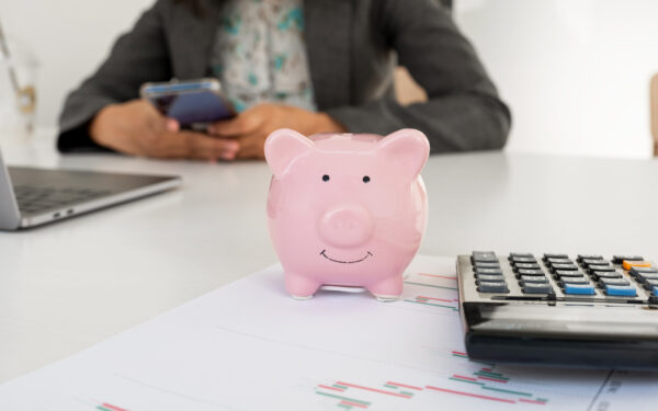 Person holding cell phone in their hands at desk with pink piggy bank calculator and papers.