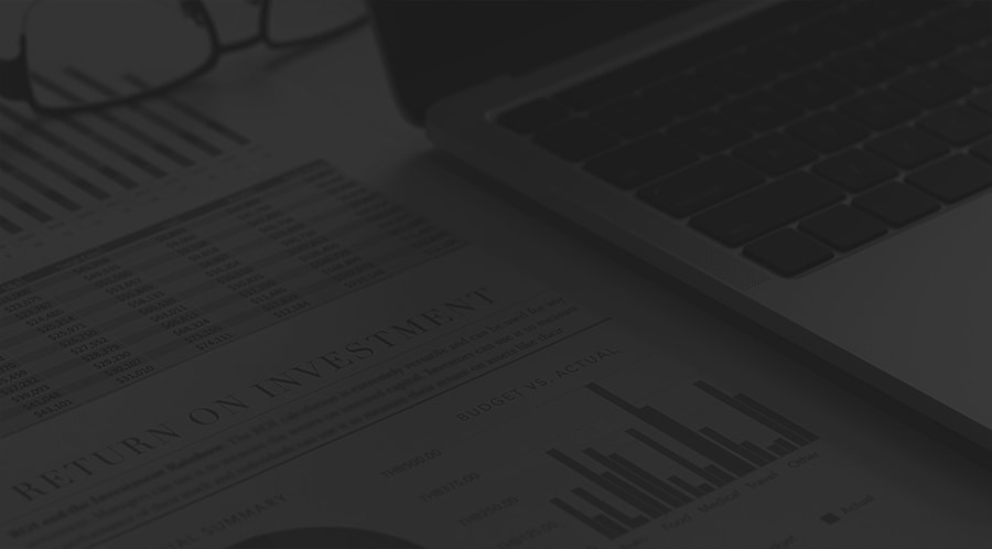 Paper with numbers and charts next to an open laptop and eyeglasses in white and gray.