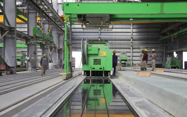 Four people wearing yellow hardhats stand near green metal industrial machine in a factory.