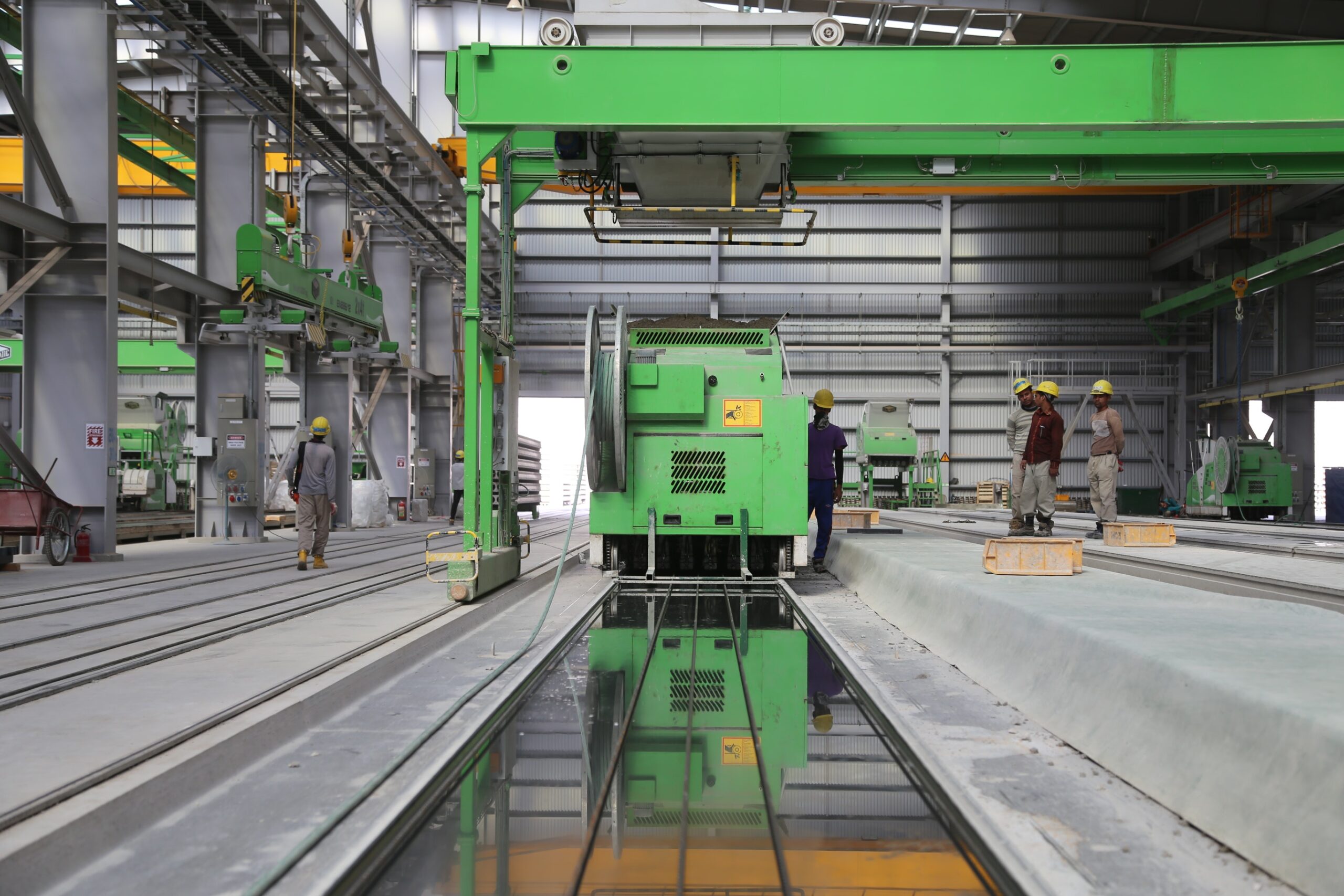 Four people wearing yellow hardhats stand near green metal industrial machine in a factory.