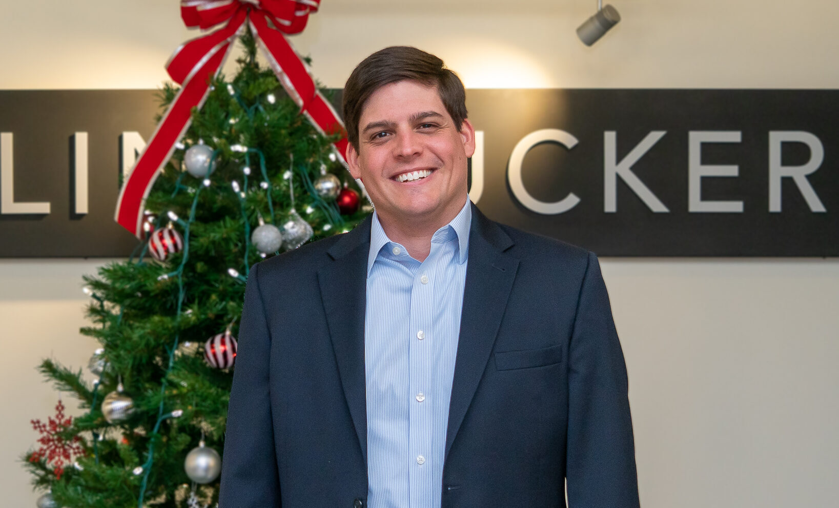 Ellin & Tucker director Zach Bromwell stands in front of Christmas tree in the Ellin & Tucker lobby.