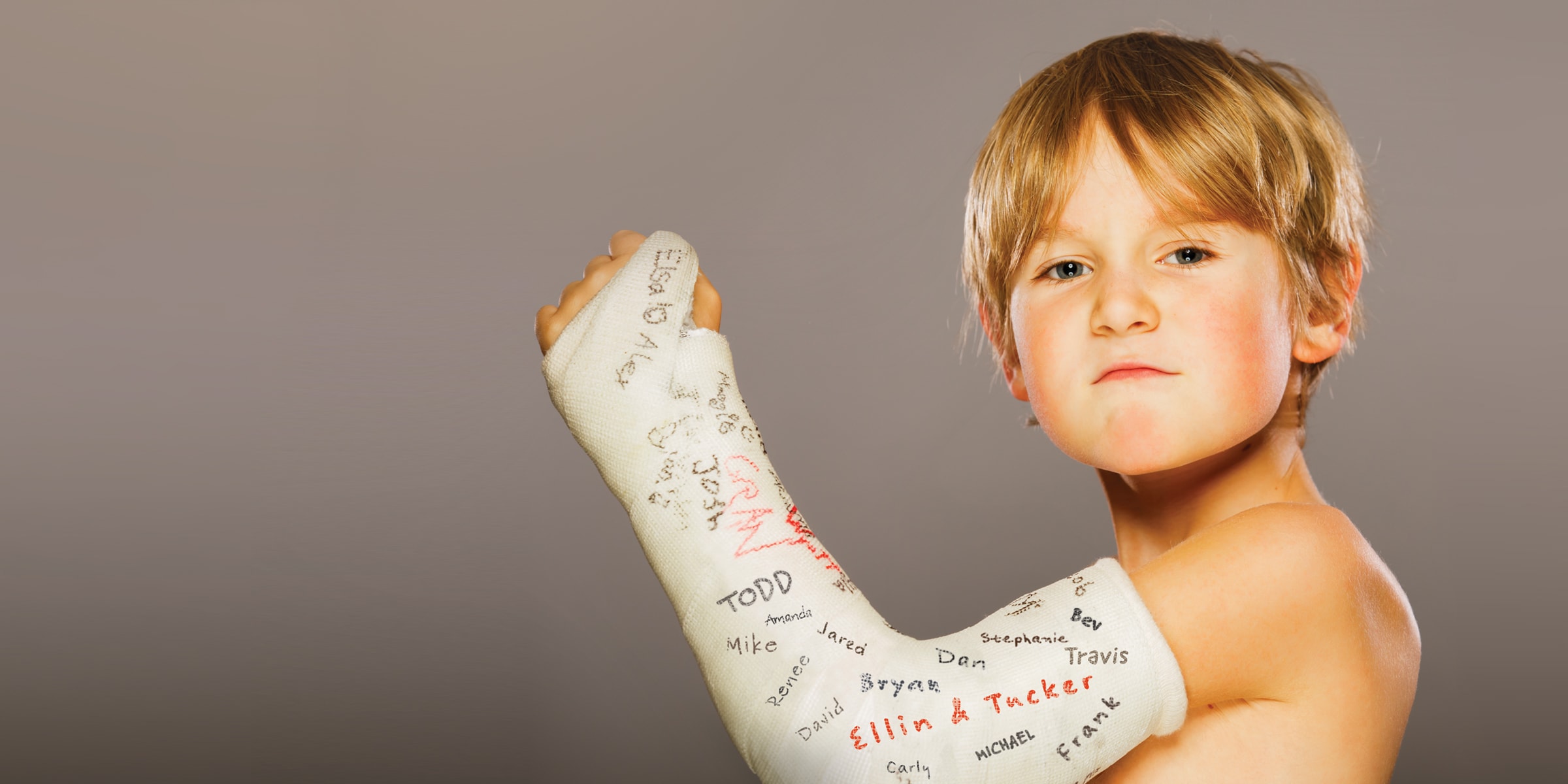 Blonde haired child making a determined face while holding up his left arm in a signed white cast.