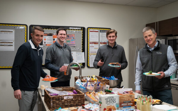 Ben Bloom Jack Mathias Andy McGinnity and Andy Herbick stand in the Ellin & Tucker kitchen holding assorted snack foods and smiling at the camera