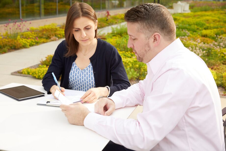 Woman and man sit on patio looking at documents on table.