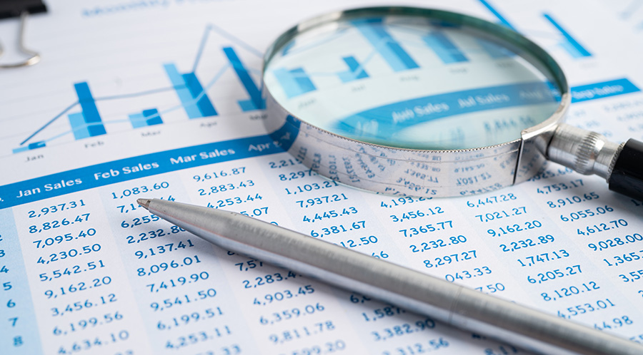 Magnifying glass and pen resting on top of paper with numbers.