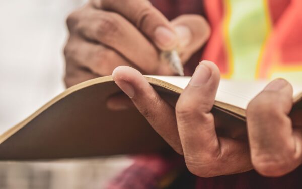 A person wearing an orange and yellow safety vest writing in a notebook.