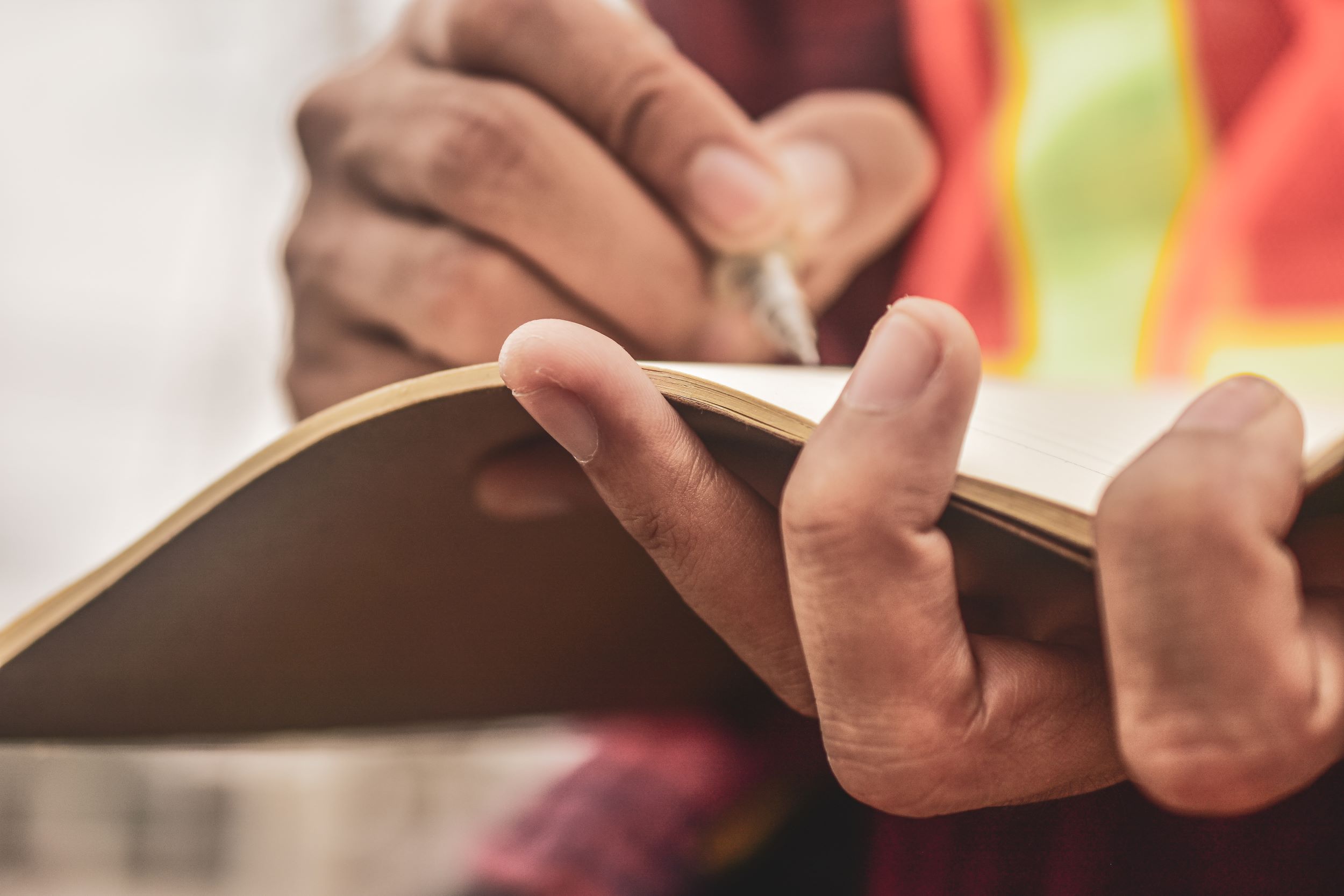 A person wearing an orange and yellow safety vest writing in a notebook.