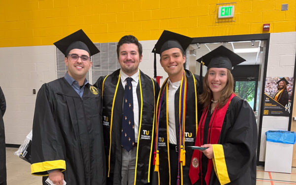 Sebastian Sorrondeguy, Nicholas Telegadas, Alexander Kouhi, and Tori Ambler stand together wearing their black graduation cap and gowns