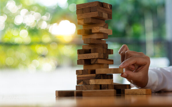 A hand pulls out a Jenga piece from the bottom portion of the tower.