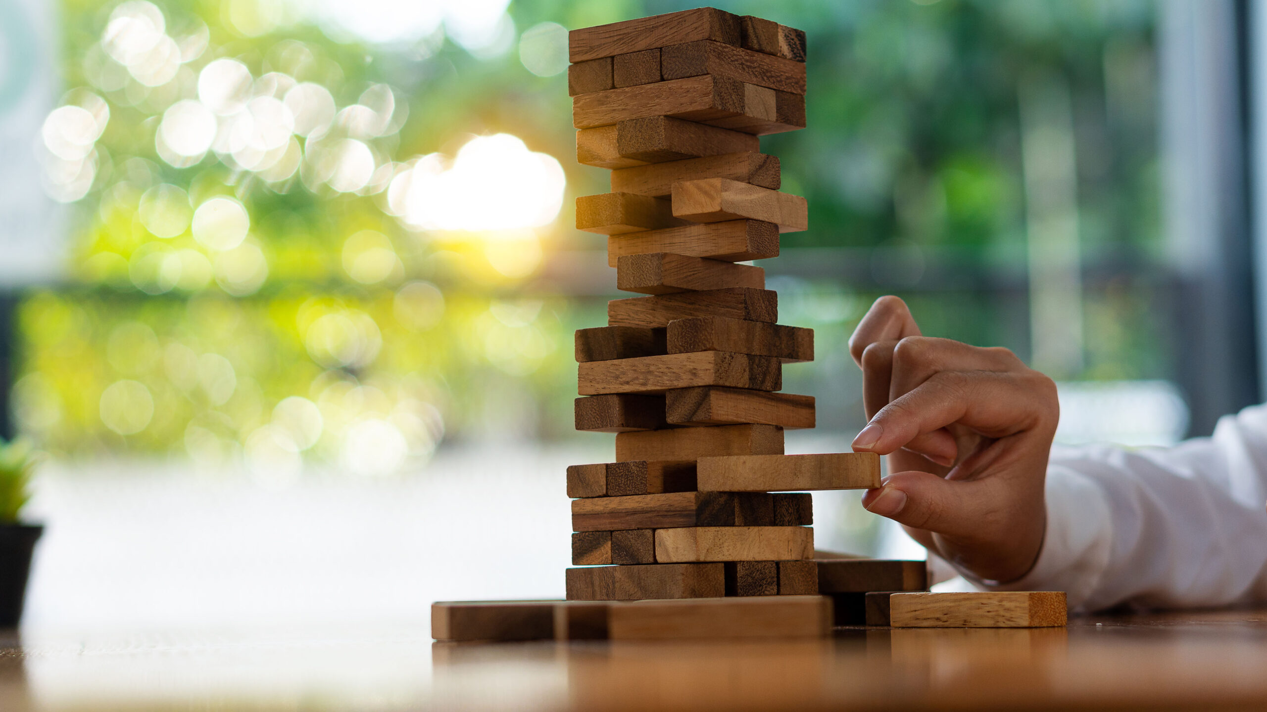 A hand pulls out a Jenga piece from the bottom portion of the tower.