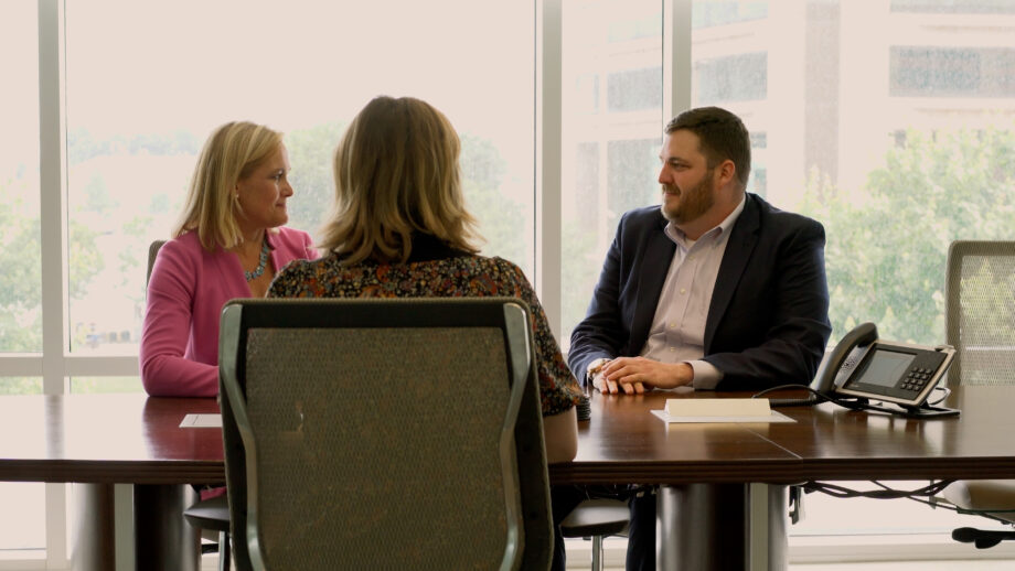 A man and a woman sit across a conference table from an interviewee.