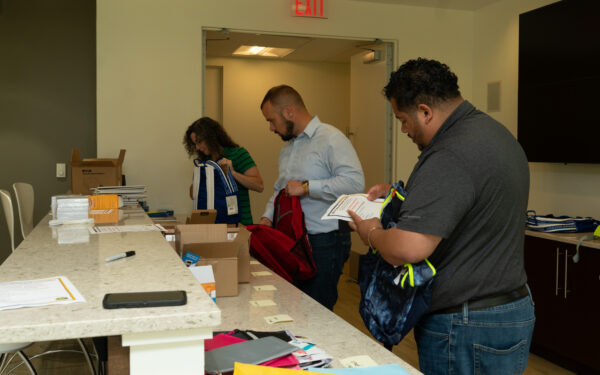 Three people fill backpacks with school supplies.