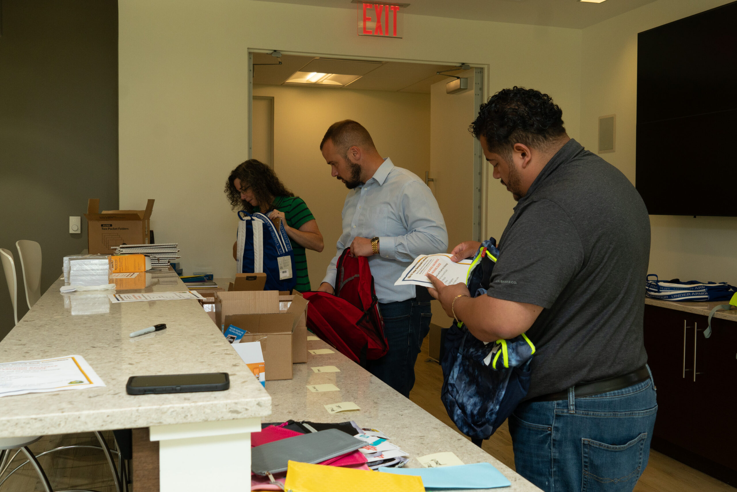 Three people fill backpacks with school supplies.