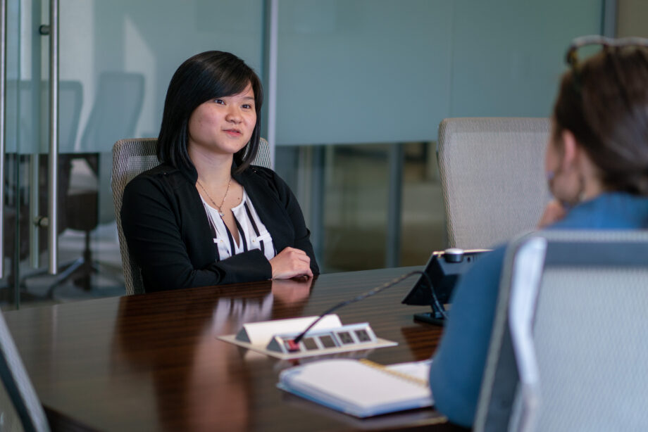 Nhu Do sits at conference table talking to another person.