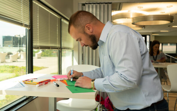 Man leaning over a table as he writes on construction paper.
