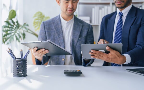 Two business men looking at a tablet while standing at a white desk.