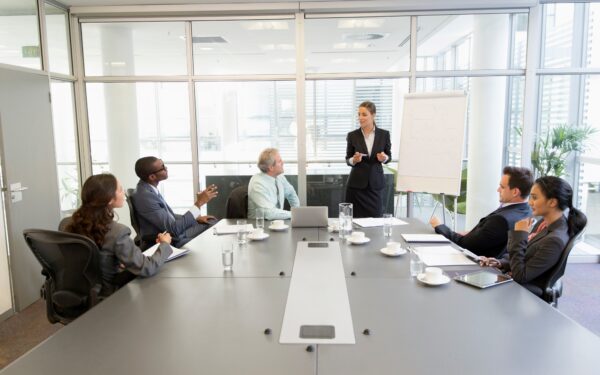 Five people sit at conference table while a person gives presentation.