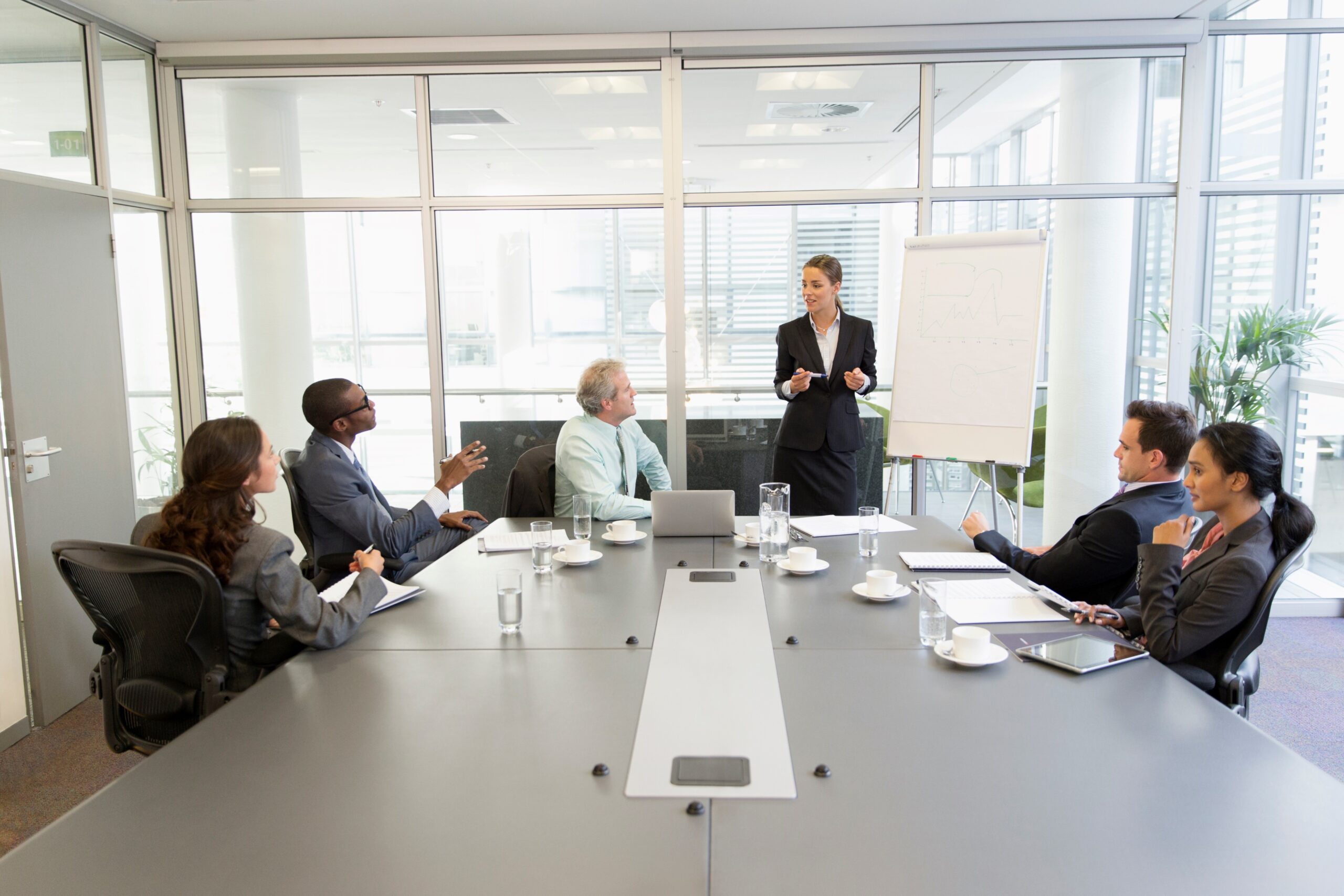 Five people sit at conference table while a person gives presentation.