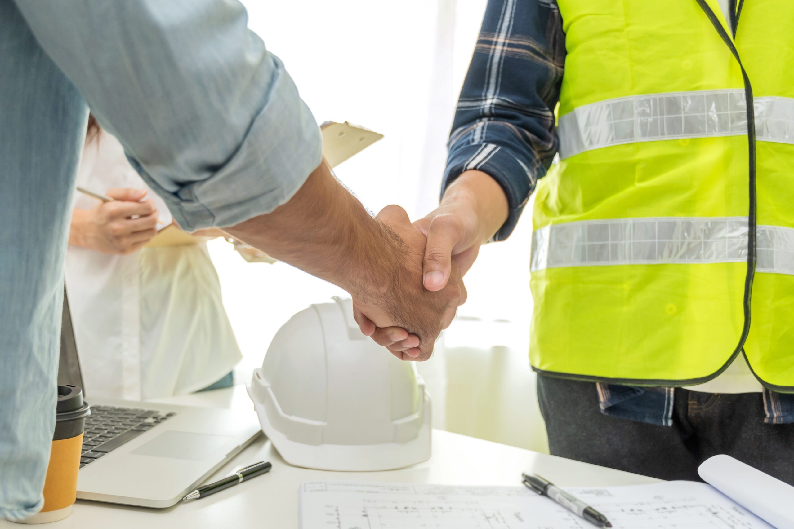 Man in yellow construction vest shakes hand of man in button up shirt