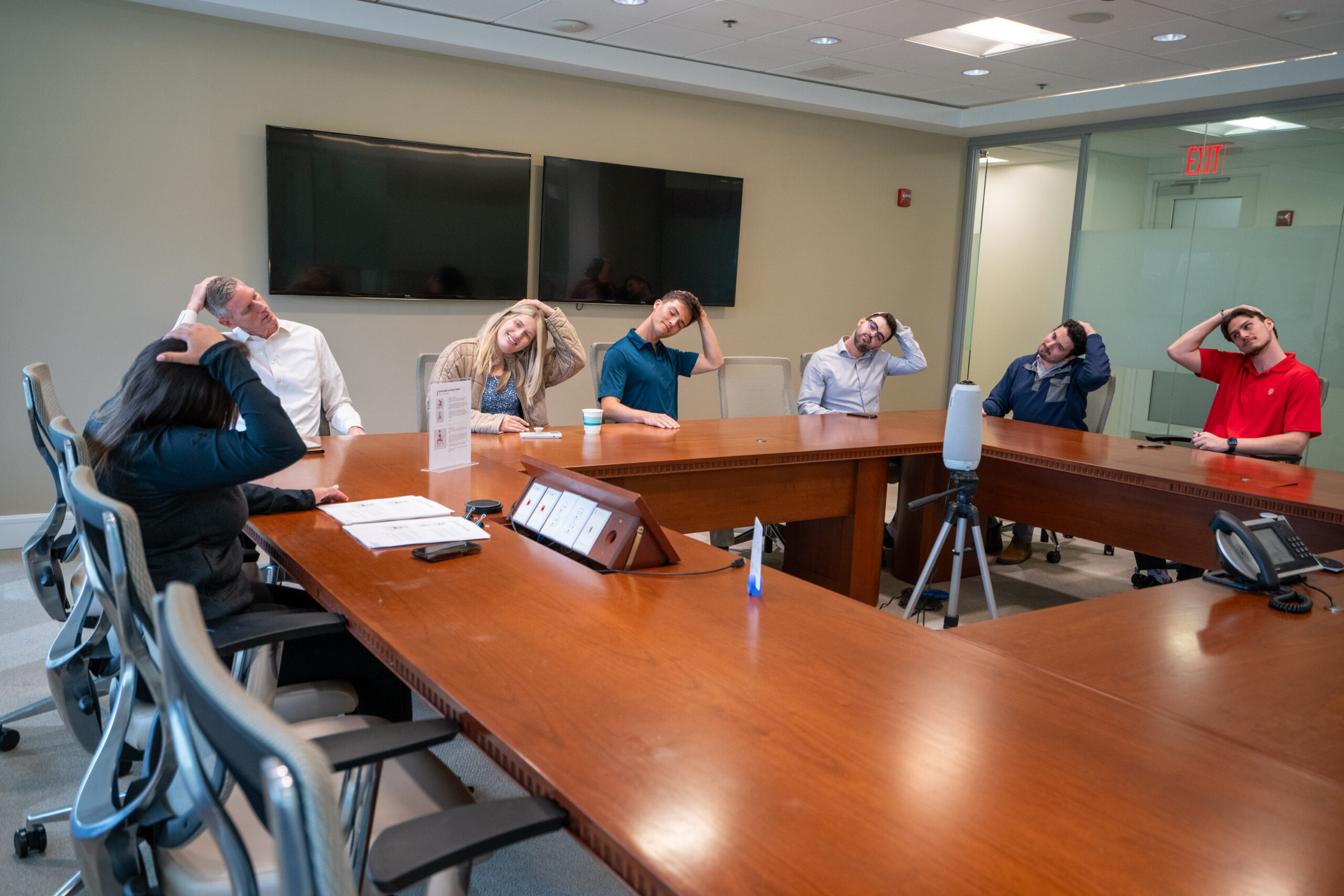 Group of people sitting at conference table stretching their necks using their hands