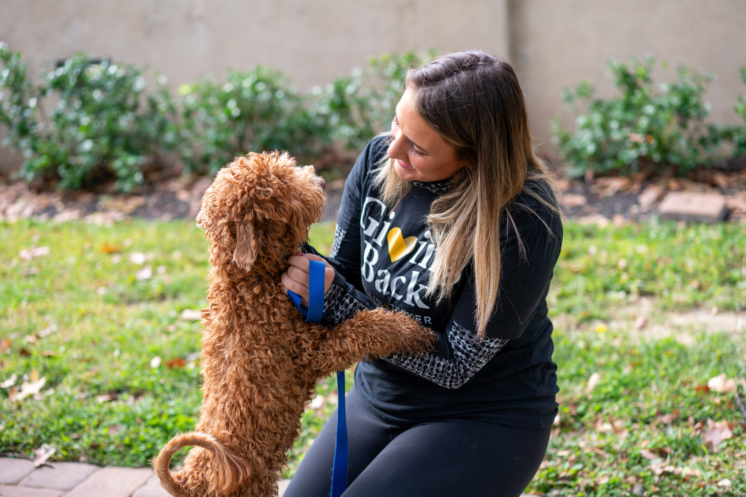 Woman kneeling on ground petting a small brown dog