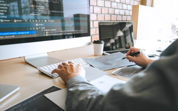 man typing on key board with large monitor and laptop on desk