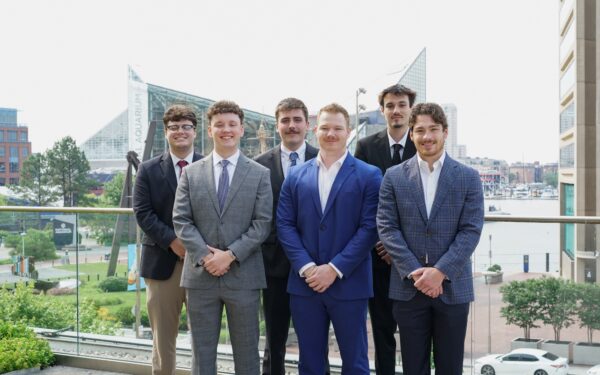 Six college age men stand on Ellin & Tucker's patio with the National Aquarium behind them