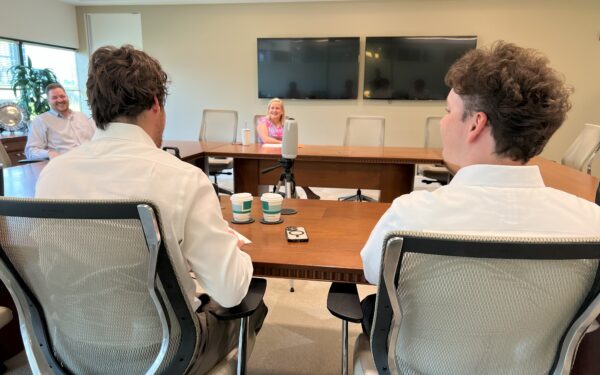 Two men in white shirts sit at table framing Aileen Eskildsen sitting across the table facing camera