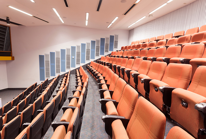rows of orange chairs in lecture hall with fluorescent lights