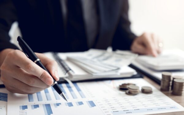 hand holding pen over papers with numbers and charts