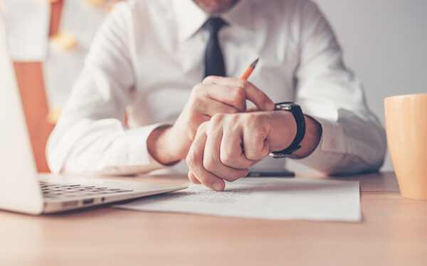 man in white b utton up shirt holding pencil at desk while checking black watch
