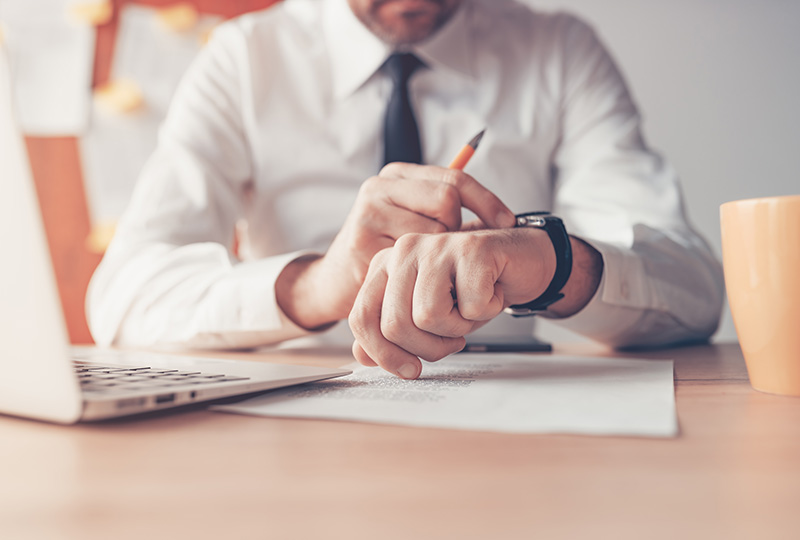 man in white b utton up shirt holding pencil at desk while checking black watch