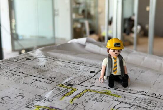 Play Mobile character in gold construction hat sits on construction blue prints